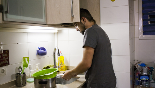 Un joven friega los platos en la cocina de su domicilio